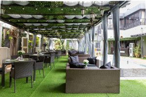 A hotel lounge featuring multiple tables surrounded by chairs, all set beneath an elegantly decorated ceiling, creating a welcoming atmosphere.